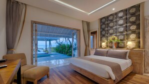 A modern bedroom with a large bed, a wooden desk, and a view of a pool and greenery.