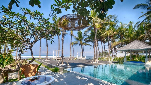 A poolside area with a clear view of the ocean, surrounded by palm trees and lounge chairs.
