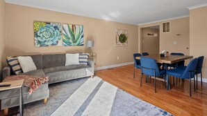 Ein Wohnzimmer mit grauem Sofa, blauen Stühlen, einem Holzesstisch und einem Streifen Teppich.