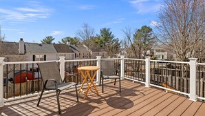 Eine Holzterrasse mit weißer Geländer, einem runden Tisch und zwei Stühlen.