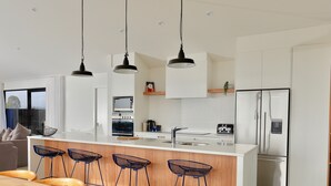 Cocina moderna con armarios blancos, una isla central con taburetes de bar, electrodomésticos de acero inoxidable e iluminación colgante.