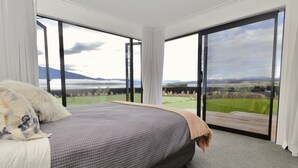Un dormitorio con una cama grande, vistas a un paisaje verde a través de puertas corredizas y una montaña al fondo.