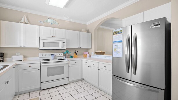 Una cocina moderna con armarios blancos, un refrigerador de acero inoxidable, un microondas y un horno.