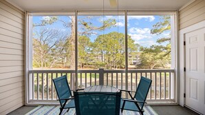 Un patio cubierto con una mesa y sillas, amplias ventanas que ofrecen vistas a árboles y edificios.