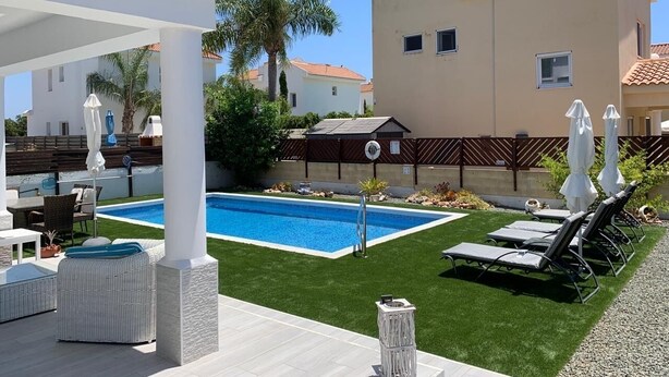 A pool area with a clear blue pool, surrounded by artificial grass, white lounge chairs, and umbrellas. - 2 bedroom detached villa with private pool in Ayia Thekla (Ayai thekla)