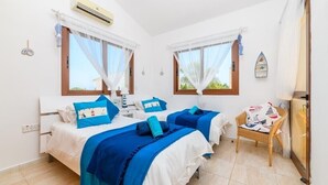 A hotel room with two beds, each with blue and white bedding, a small table with a chair, and a window with a view of greenery. - 2 bedroom detached villa with private pool in Ayia Thekla (Ayai thekla)