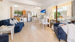 A spacious living area with a sofa set, a dining table, and a kitchen in the background. - 2 bedroom detached villa with private pool in Ayia Thekla (Ayai thekla)