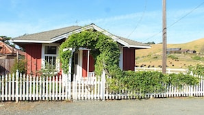 Una casa rossa con un recinto bianco a stecche, un garage e un piccolo portico.