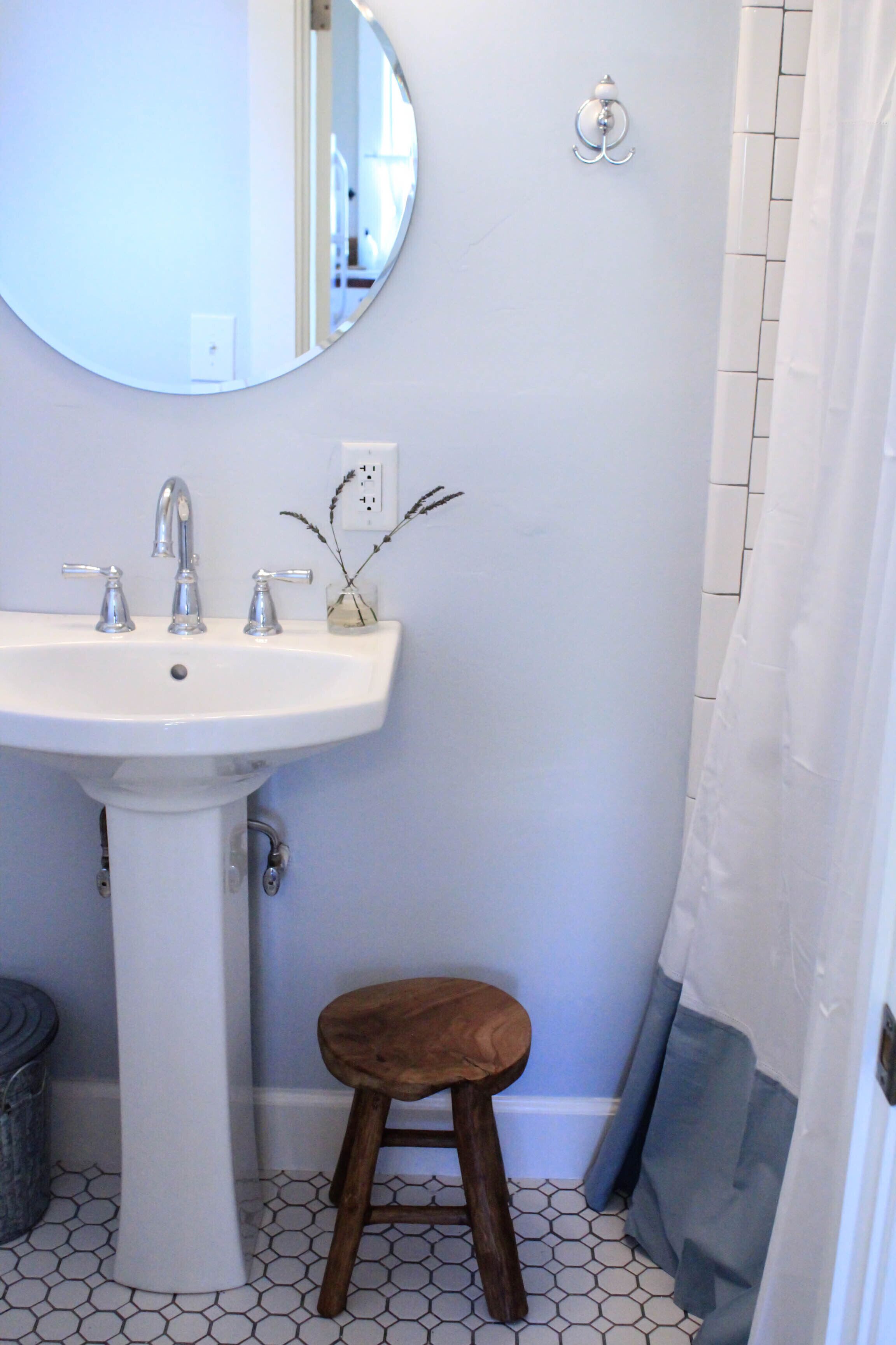 A bathroom with a white sink, two faucets, a mirror, and a wooden stool.