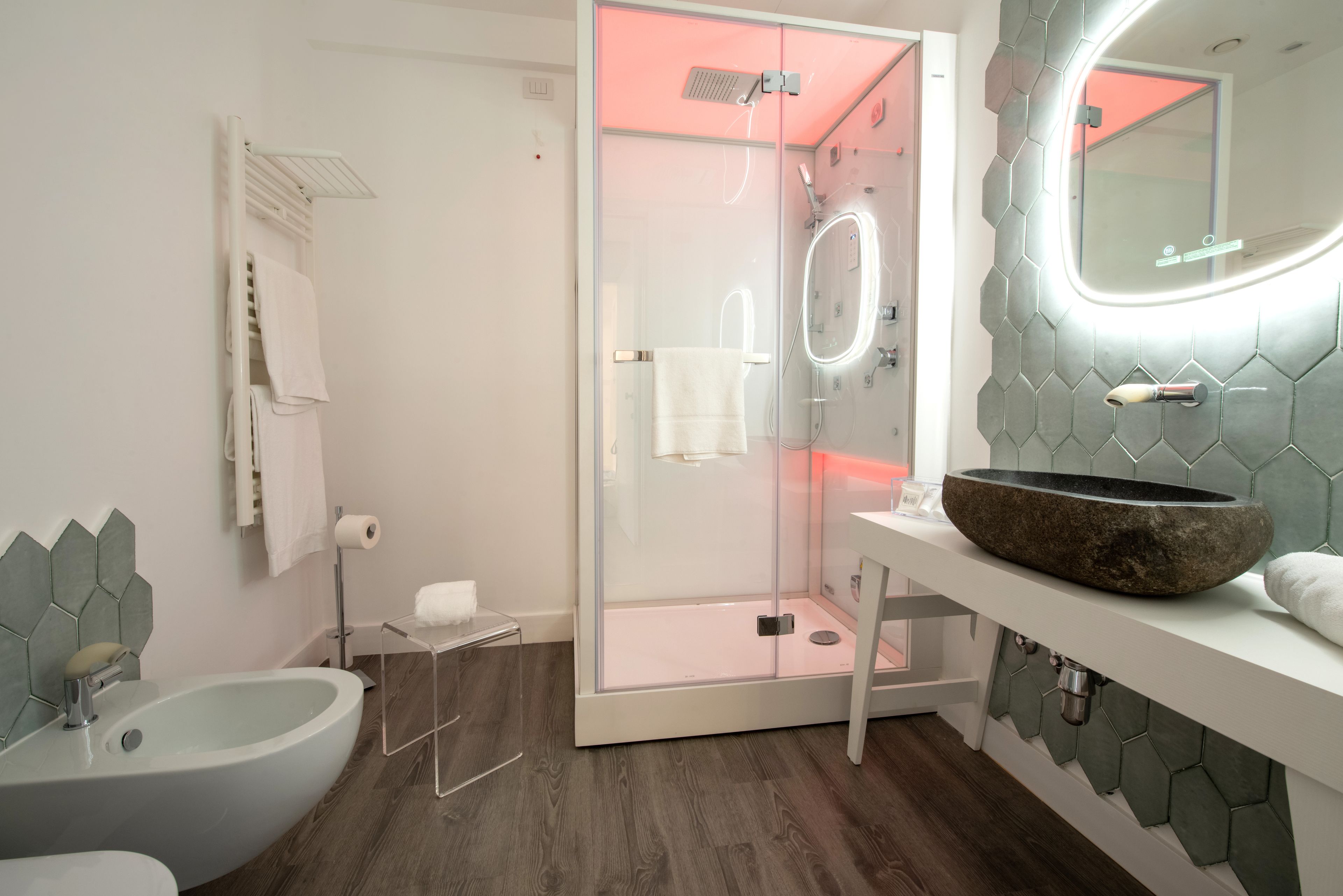 Een moderne badkamer met een douchecabine van glas, een wastafel op een zuil en een meubel met een rond wastafelbakje.