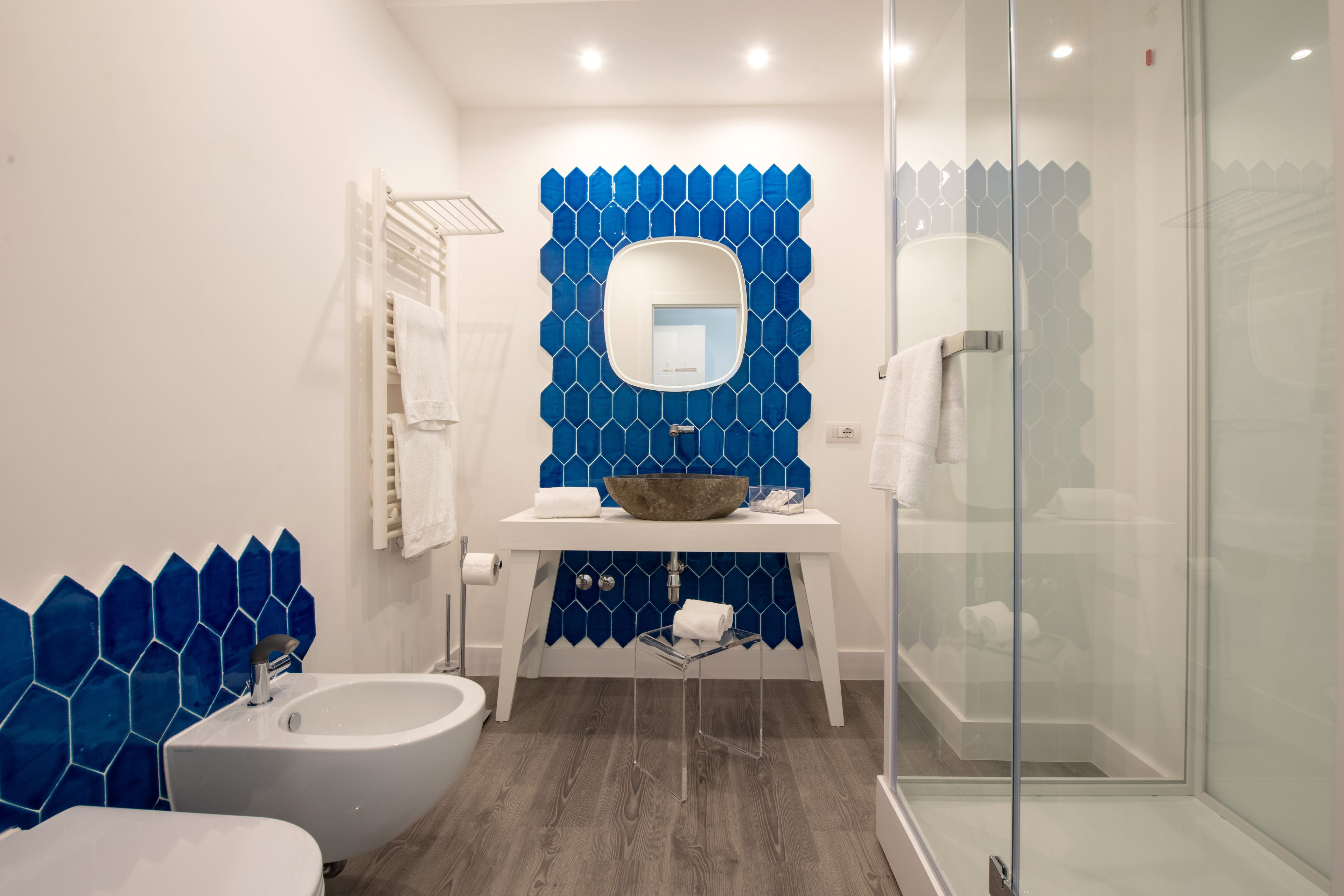A modern bathroom with a white sink, a large mirror, and a blue hexagonal tile backsplash.