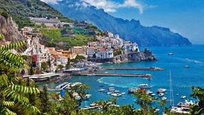 Una pittoresca cittadina costiera, con edifici colorati, un porto e numerose imbarcazioni, e montagne sullo sfondo.