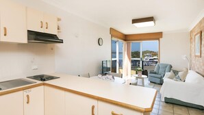 Une cuisine moderne dotée d’une cuisinière intégrée, un coin repas avec une table et des chaises, un canapé et une vue sur les bateaux à travers une porte vitrée.