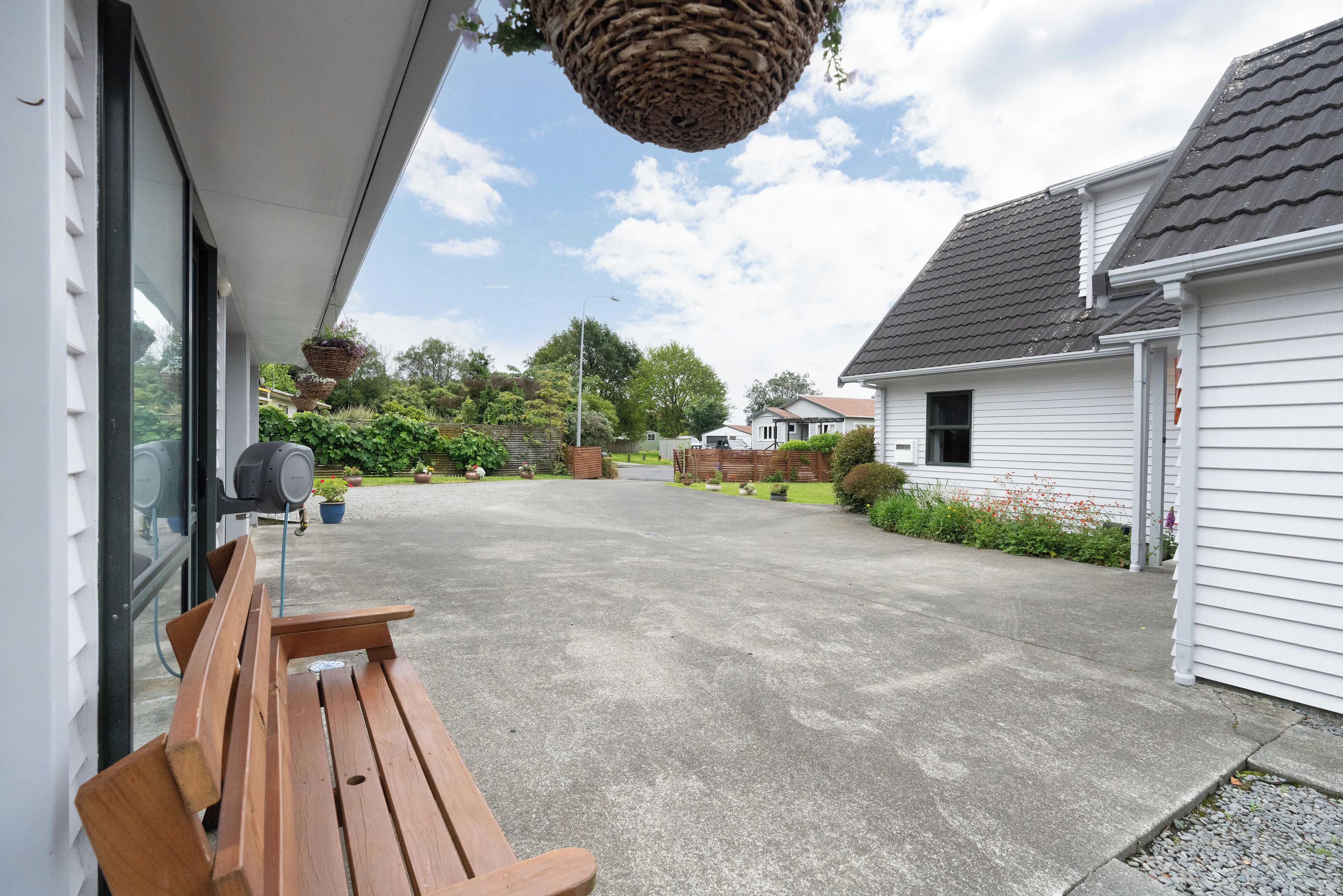 A covered outdoor area with a bench, a hanging basket, and a view of a residential street.
