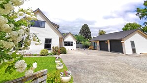 A residential area with a driveway leading to a house with a garage. There are potted plants along the driveway and a wooden fence on the left. - Atarau Grove  Studio (Paraparaumu)