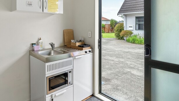 A compact kitchen with a built-in oven, microwave, and sink, a wooden cutting board, and a small countertop with a kettle and a box of tissues. - Atarau Grove  Studio (Paraparaumu)