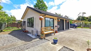 A single-story house with a porch, a bench, and a car parked in the driveway. - Atarau Grove  Studio (Paraparaumu)