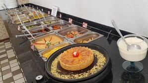 A buffet with various food options, including a cake with a cherry on top, and a bowl of soup. - Apartment in Ondina on the carnival circuit (Salvador)