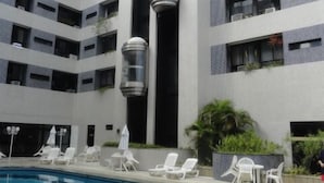 A pool area with lounge chairs and umbrellas, surrounded by a building with multiple balconies and windows. - Apartment in Ondina on the carnival circuit (Salvador)