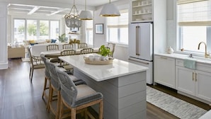 Una cocina moderna con armarios blancos, una isla central con taburetes y luces colgantes, con vistas al área de comedor.