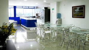 A modern kitchen with a blue accent wall, white cabinets, and a water dispenser. There are several round tables with metal chairs, and a painting is visible on the wall. - Hotel Aussie Koala (Armenia)