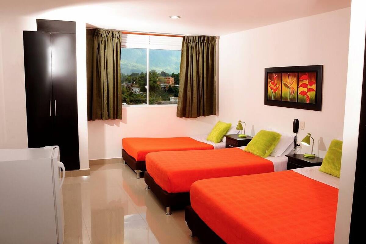 A hotel room with three beds, a wardrobe, a desk, and a window with curtains.