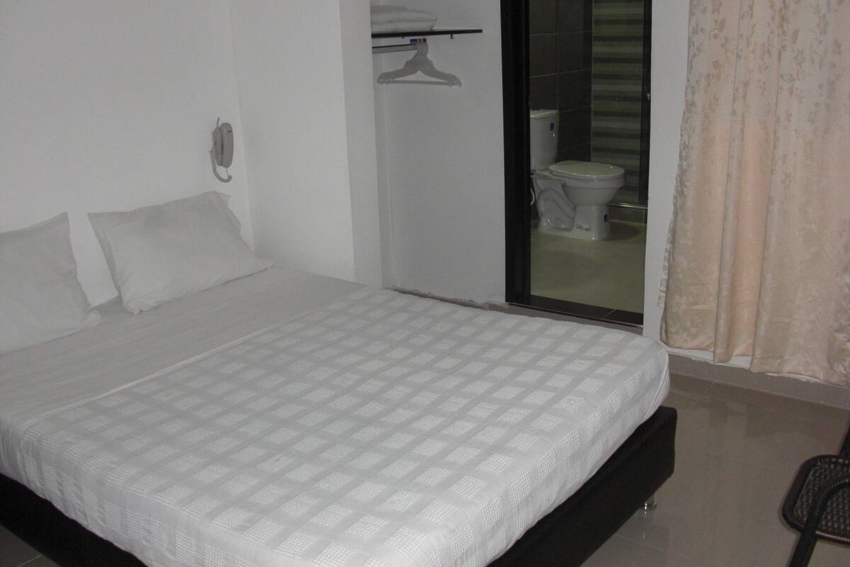 A bedroom with a bed, a hanging telephone, a bathroom with a toilet, and a shower area.