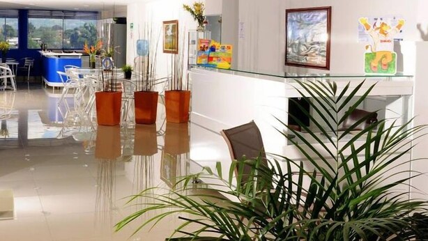 A modern reception area with a glass counter, white walls, and a view of the outdoors through large windows. - Hotel Aussie Koala (Armenia)