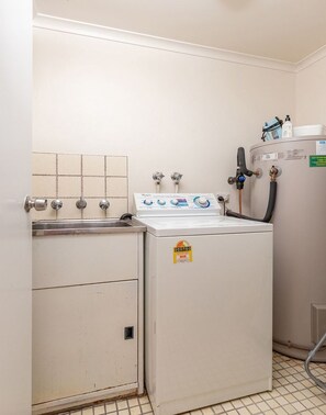 Une petite buanderie équipée d’un lave-linge, d’un évier et d’un chauffe-eau.