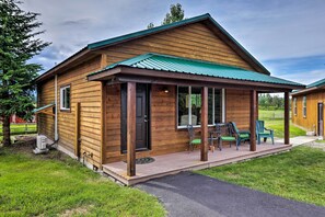 Een houten hutje met een veranda, een tafeltje en twee stoelen.