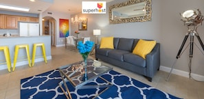 A modern living room with a grey sofa, yellow cushions, a glass coffee table, and a blue patterned rug.