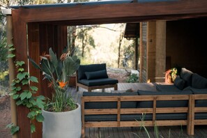 A wooden deck with a sofa and chairs, surrounded by greenery and a potted plant. - Corymbia Cottage – Broke's Secluded Escape (Broke)