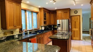 A modern kitchen with wooden cabinets, granite countertops, stainless steel appliances, and a large window providing natural light. - Cliff View Loj Home is in a Quiet Neighborhood Walking Distance to Mirror Lake. (Lake Placid)