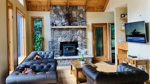 A spacious living room with a stone fireplace, wooden ceiling, and large leather sofas. - Cliff View Loj Home is in a Quiet Neighborhood Walking Distance to Mirror Lake. (Lake Placid)