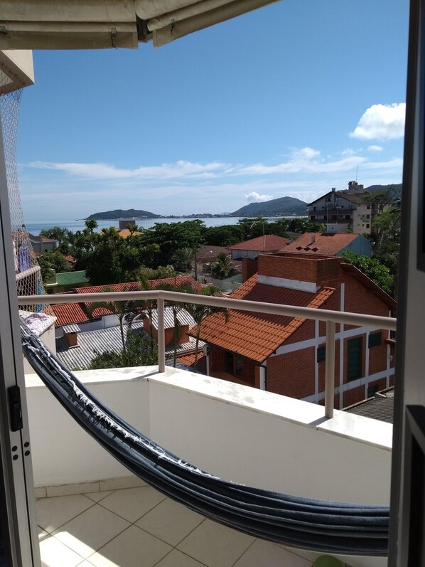 A balcony with a view of a coastal town, buildings with red-tiled roofs, and a clear sky.