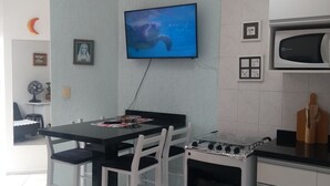 Una cocina moderna con armarios blancos, una estufa a gas y un microondas. Hay una mesa de comedor con sillas y un televisor de pantalla plana montado en la pared.