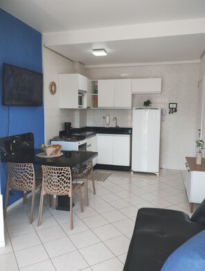 A compact kitchen with white cabinets, a black countertop, and a dining area with two chairs. - Apartment 50m from Cachoeira Beach - Balcony with BBQ, Air Conditioning and WiFi (Cachoeira do Bom Jesus)
