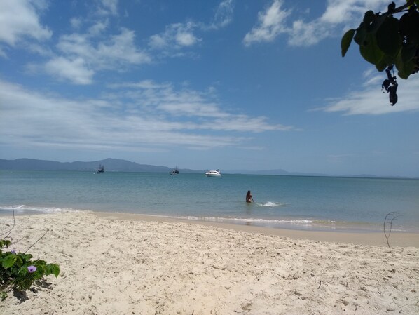 A beach with a clear sky, calm sea, and distant boats. - Apartment 50m from Cachoeira Beach - Balcony with BBQ, Air Conditioning and WiFi (Cachoeira do Bom Jesus)