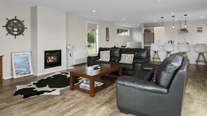A modern living room with a fireplace, leather sofas, a coffee table, and a dining area with white chairs.