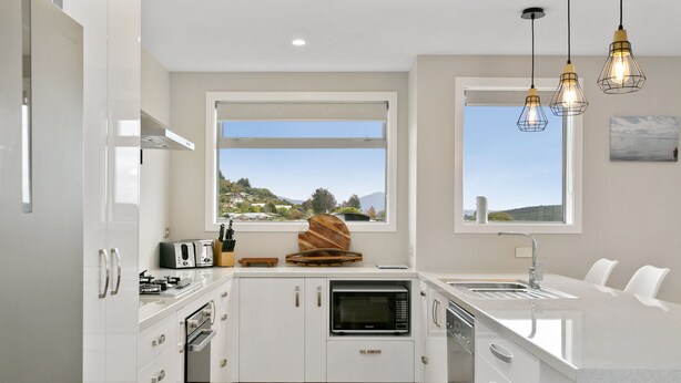 A modern kitchen with white cabinetry, a built-in microwave, and a large window offering a view of the outdoors.