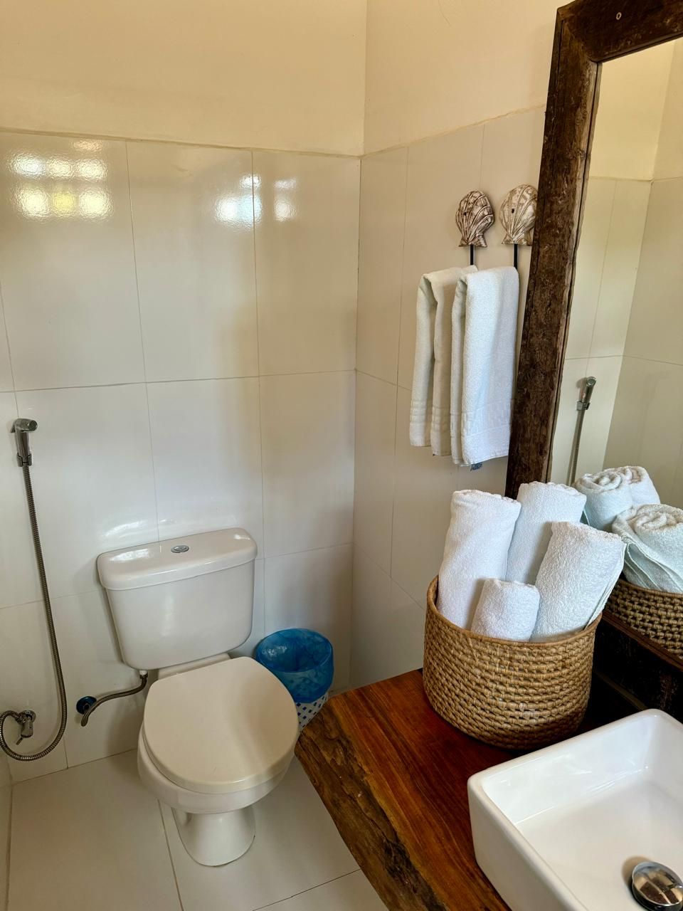 Ein Badezimmer mit Toilette, Bidet und Waschbecken. Ein Holzkosmetikschrank mit einer Korb voller Handtücher und einem Spiegel über dem Waschbecken.