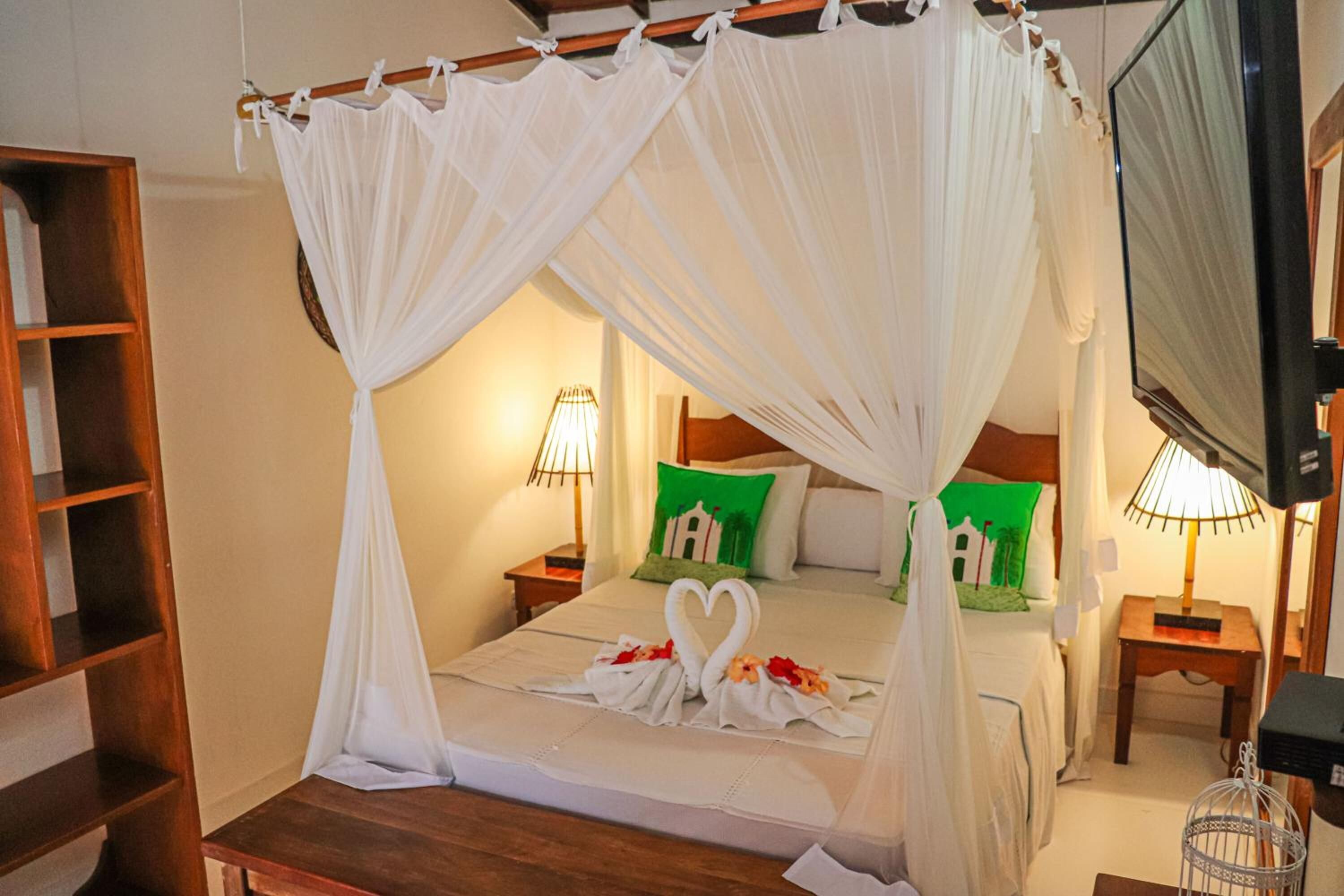 A bedroom with a four-poster bed, green pillows, and a heart-shaped decoration on the bed.