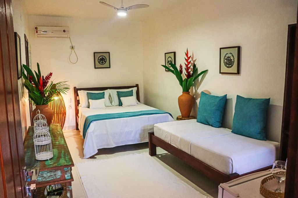 A bedroom with two beds, a wooden nightstand, a vase with plants, and framed pictures on the wall.
