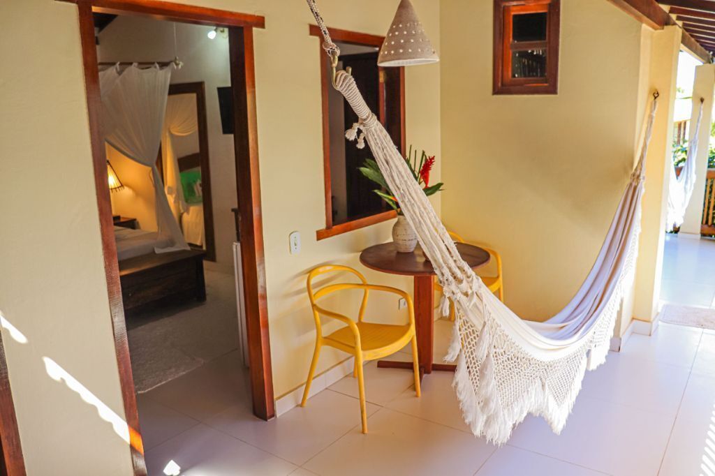 Una habitació amb un llit, una taula petita amb una cadira, un hamaca penjant i una finestra amb vistes.
