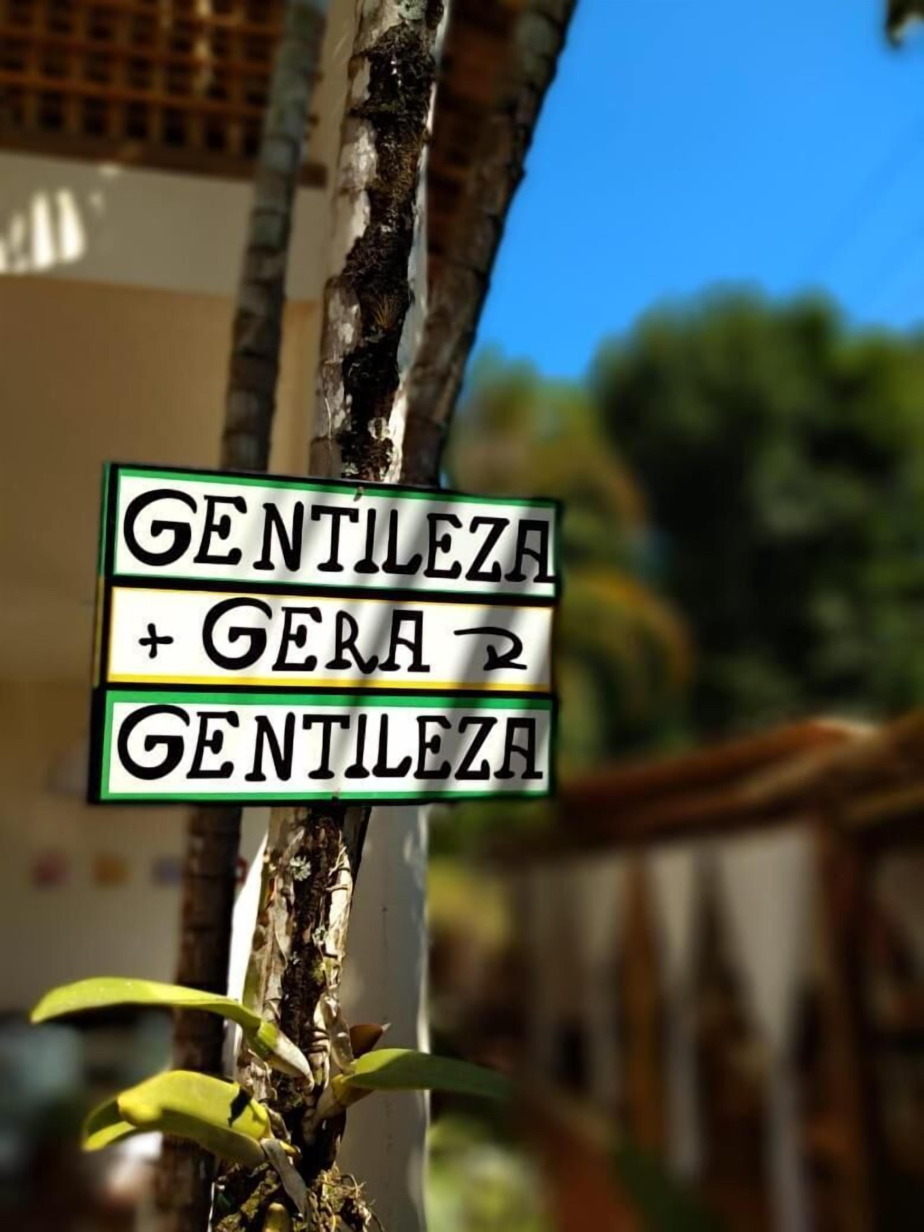 Une pancarte portant l’inscription « GENTILEZA + GERA 2 GENTILEZA » est fixée à un arbre.