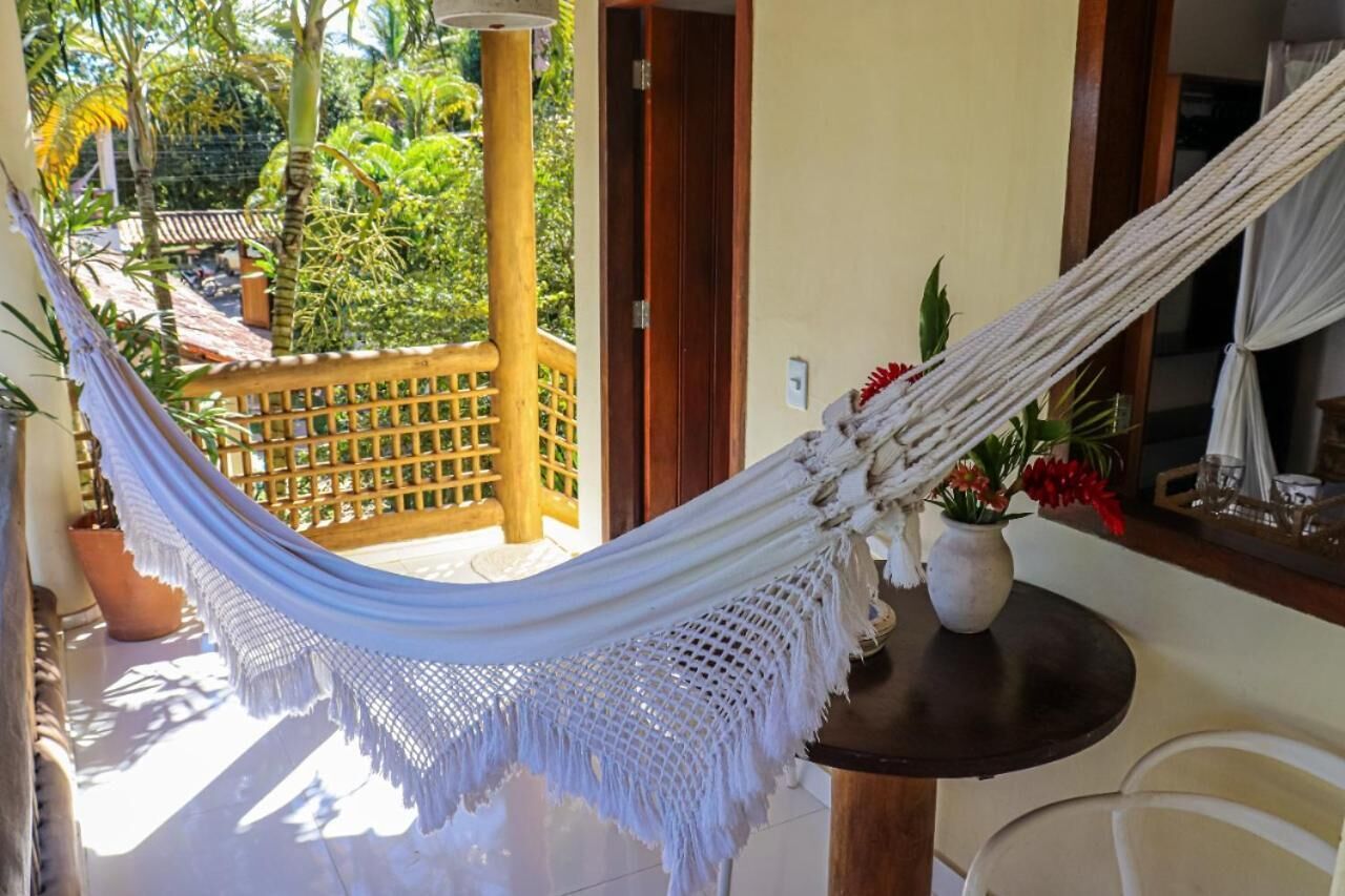 A hammock on a balcony with a view of a garden and a wooden fence.