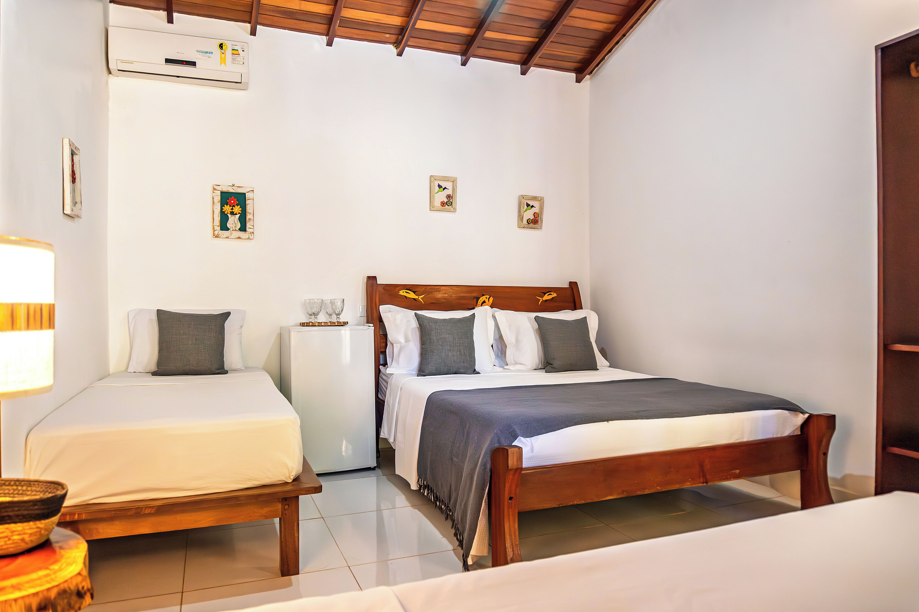 A bedroom with two beds, a wooden headboard, a small bedside table, and a wall-mounted air conditioner.