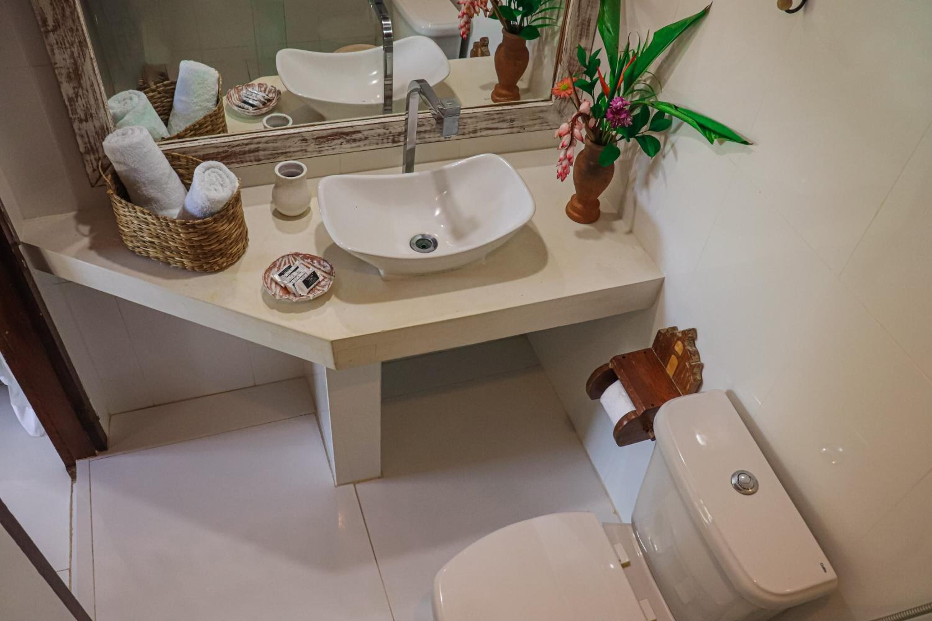 A bathroom with a white sink, a toilet, and a mirror. There are towels in a basket and a plant on the counter.