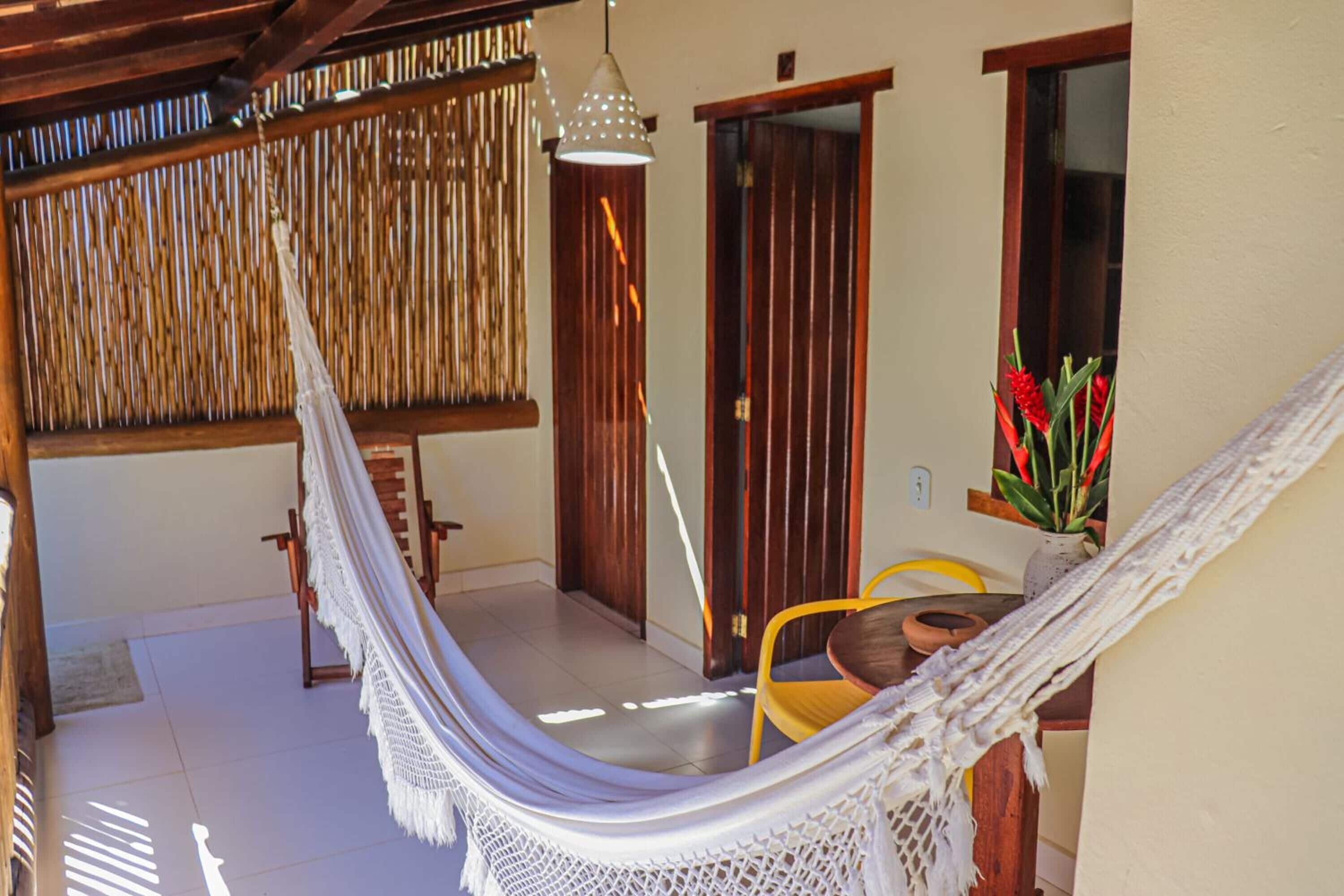 A hammock in a sunlit room with a wooden chair, a small table, and a potted plant.