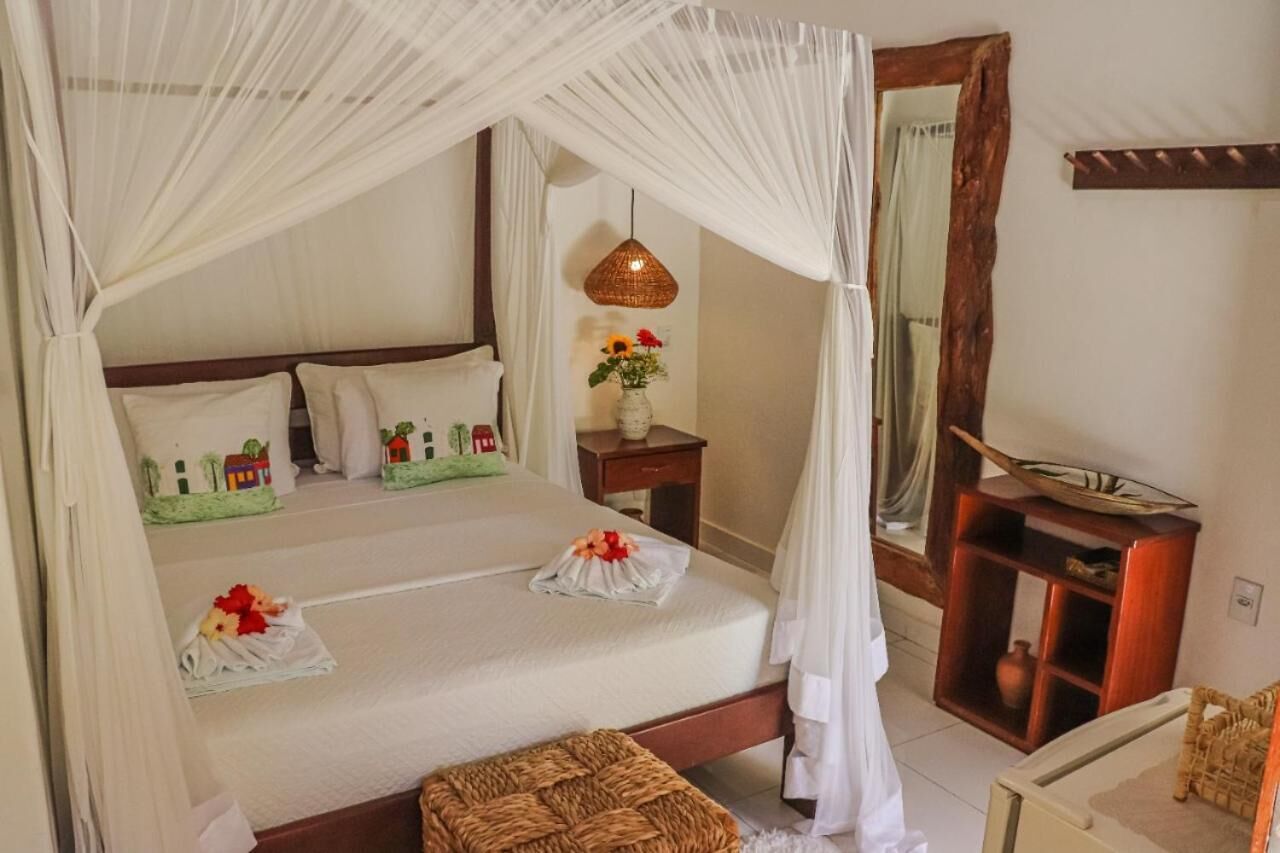 A bedroom with a canopy bed, a bedside table with a lamp, a mirror, and a small wooden cabinet.